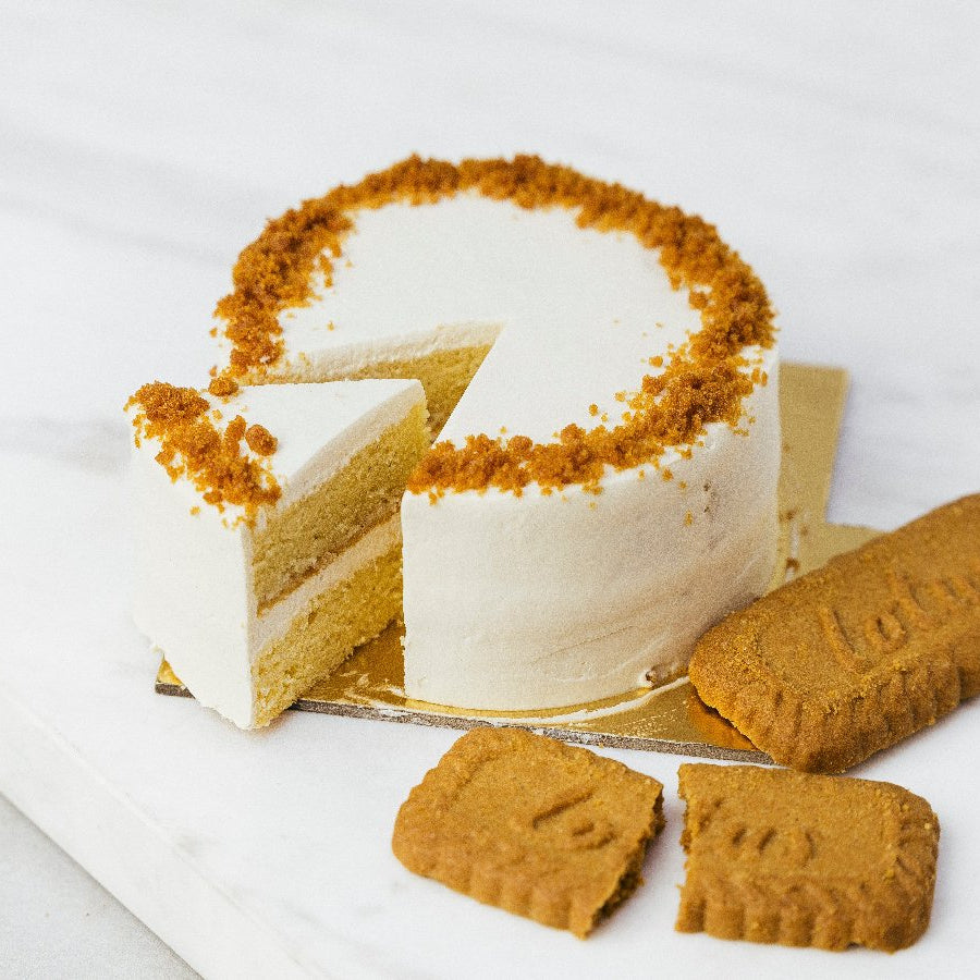 A slice of honey lotus bento cake with white frosting and golden lotus-shaped cookies on a marble surface.