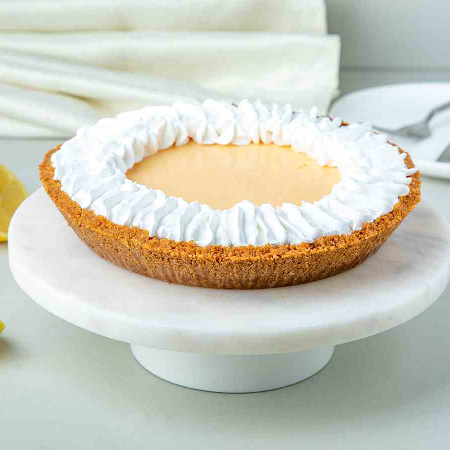 An 8-inch key lime pie with whipped cream on top, served on a white cake stand.
