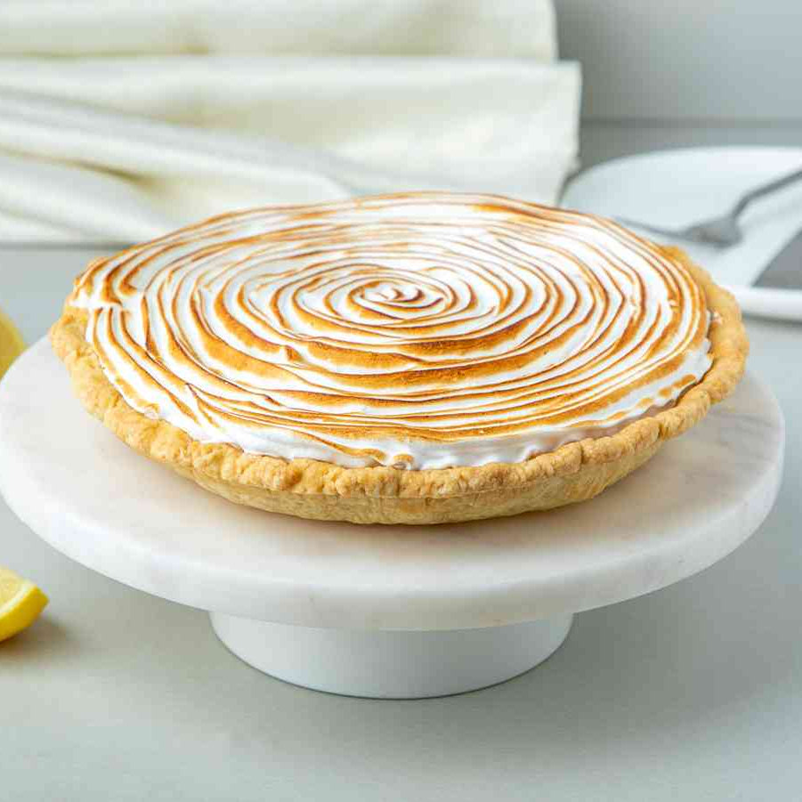 An 8-inch lemon meringue pie on a white plate with a spiral meringue topping, garnished with lemon slices and a napkin in the background.
