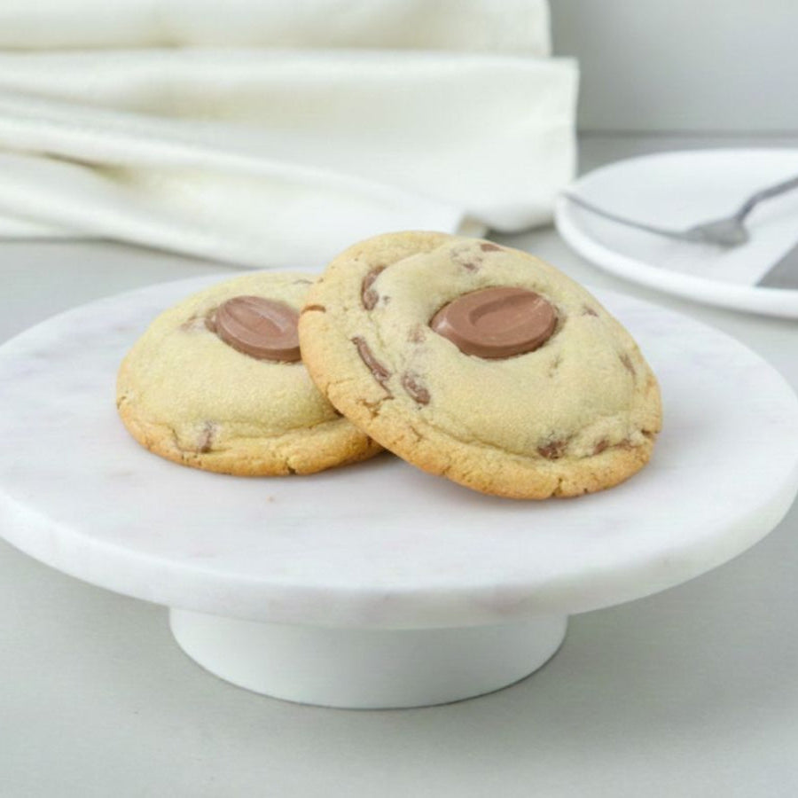 Two cookies with chocolate chips on a white marble cake stand.