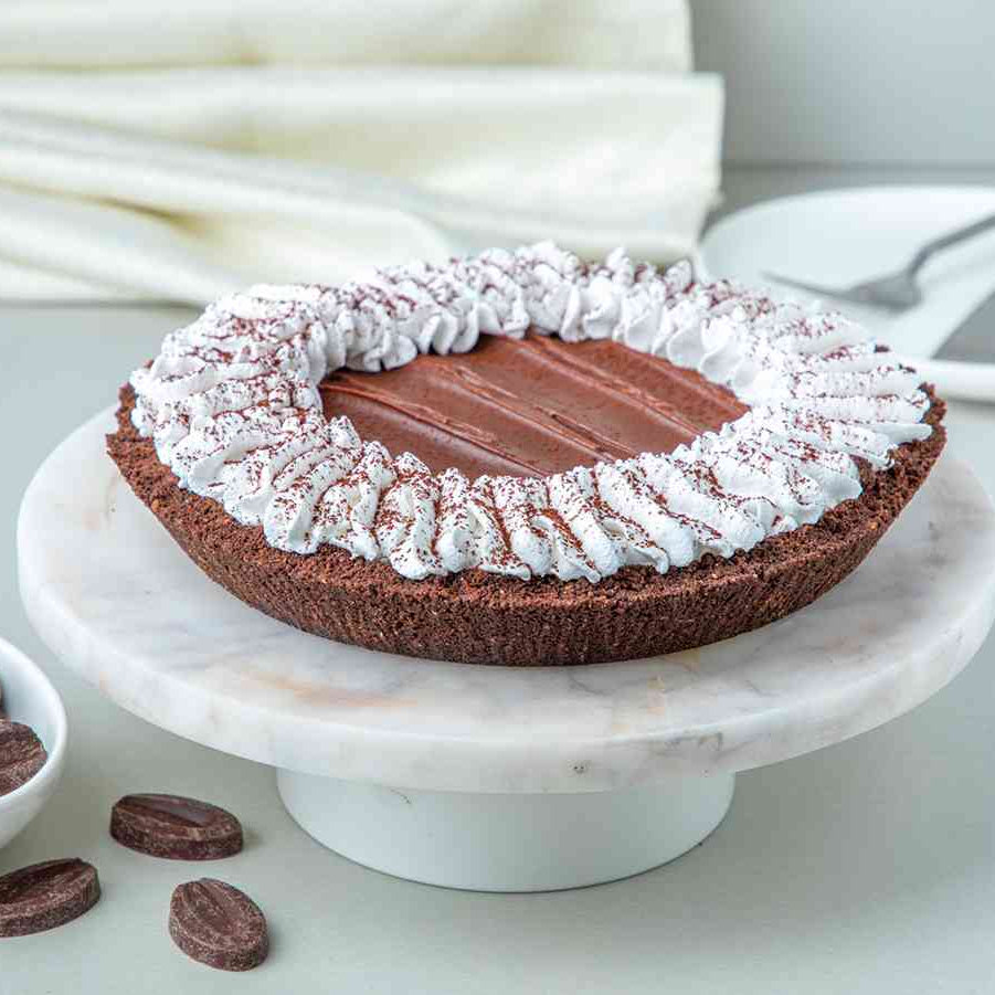 A chocolate Mississippi Mud Pie with a crumbly cookie crust, goeey chocolate center, and rich sauce on top, garnished with whipped cream, on a white plate with chocolate cookies around it.