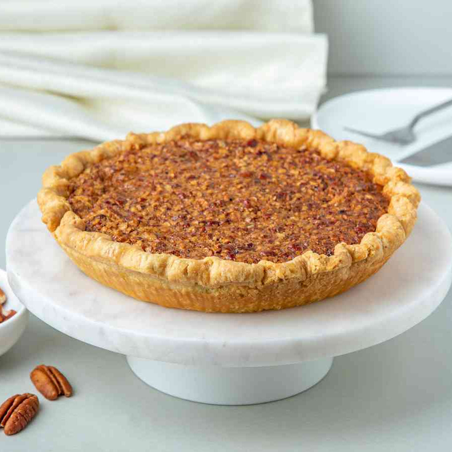 A whole pecan pie on a white plate with a few pecans scattered around, possibly indicating homemade filling.