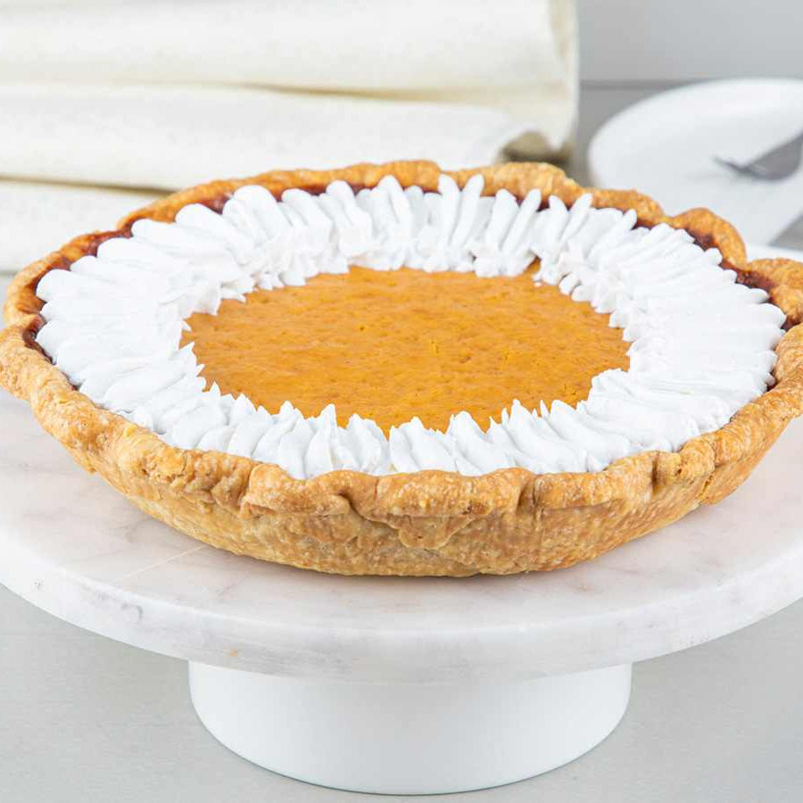An 8-inch pumpkin pie with a decorative white border on top, placed on a white plate.